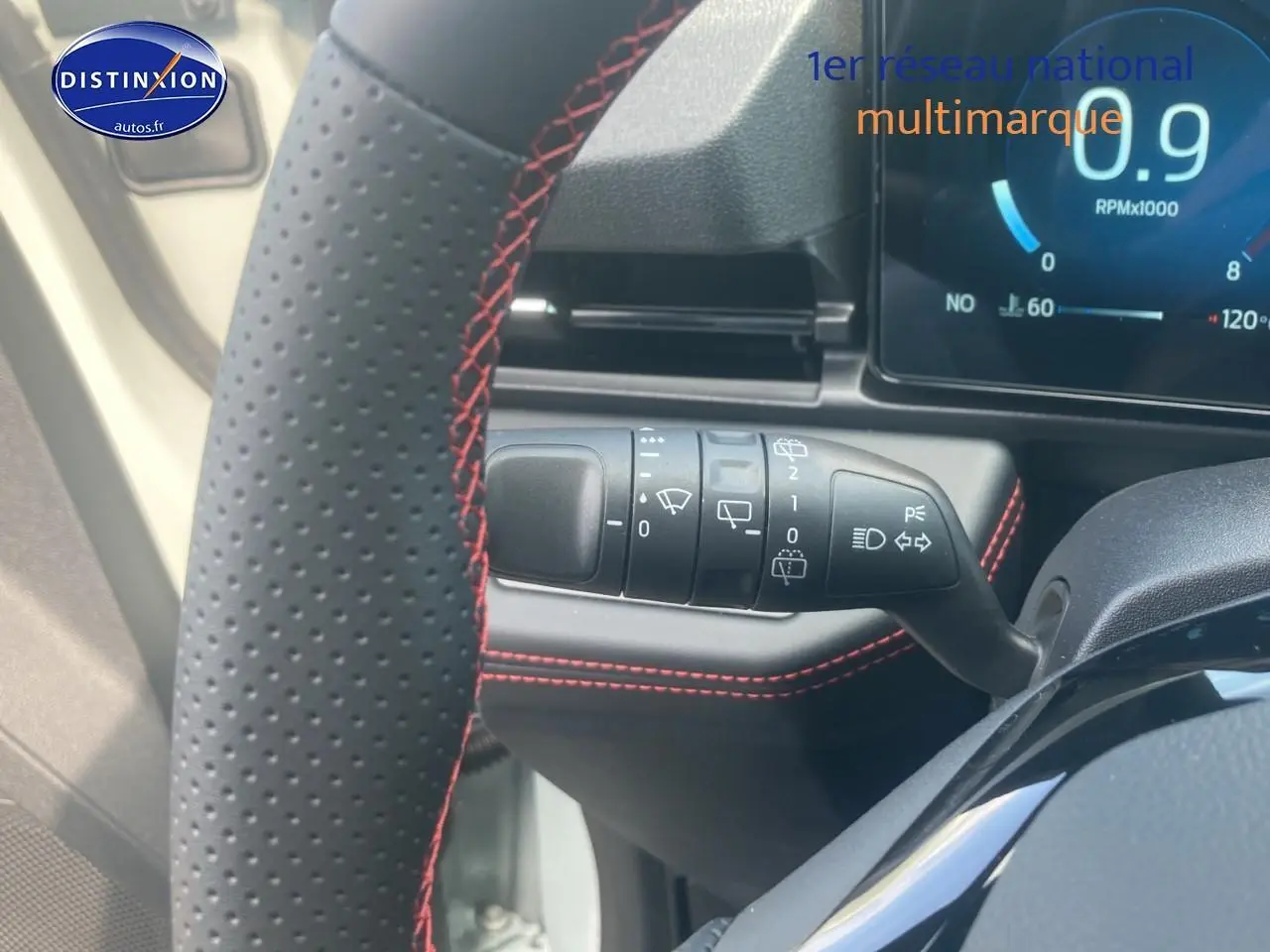 Gros plan sur le volant perforé noir avec surpiqûres rouges et la commande des essuie-glaces du Ford Puma gris cactus 2025.