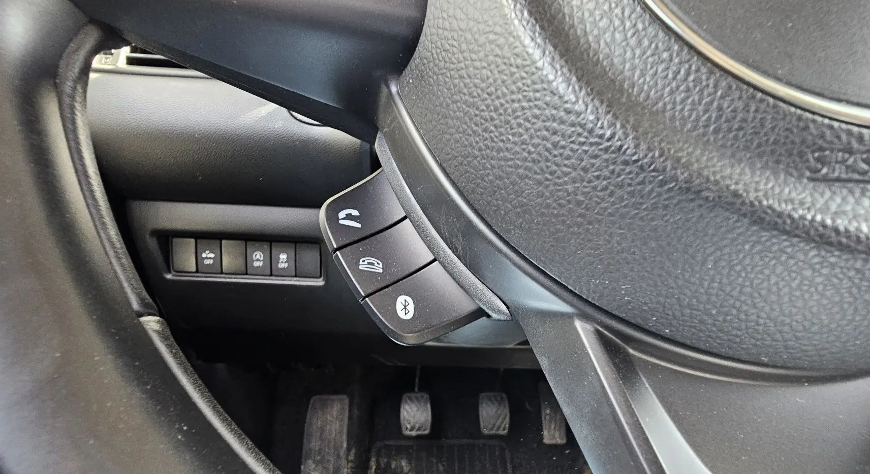 Gros plan sur le volant noir de la Suzuki Swift 2023, montrant les commandes Bluetooth et téléphone côté gauche.