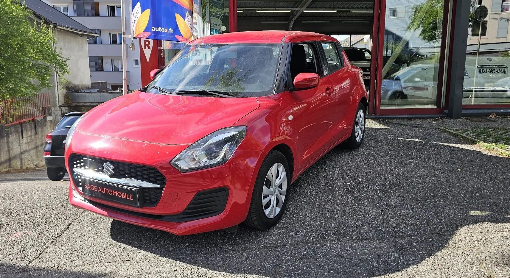 Suzuki Swift 1.2 Dualjet Hybrid rouge fervent vue 3/4 avant droit sur parking extérieur.