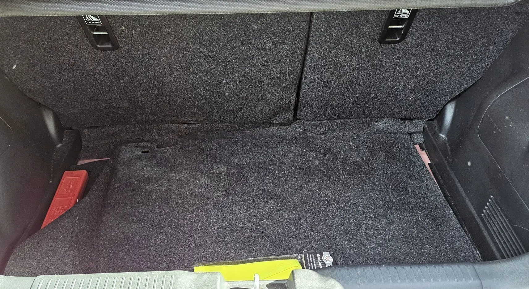 Coffre spacieux de la Suzuki Swift 1.2 Dualjet Hybrid 2023 en rouge Fervent, avec tapis noir et rangement intégré.