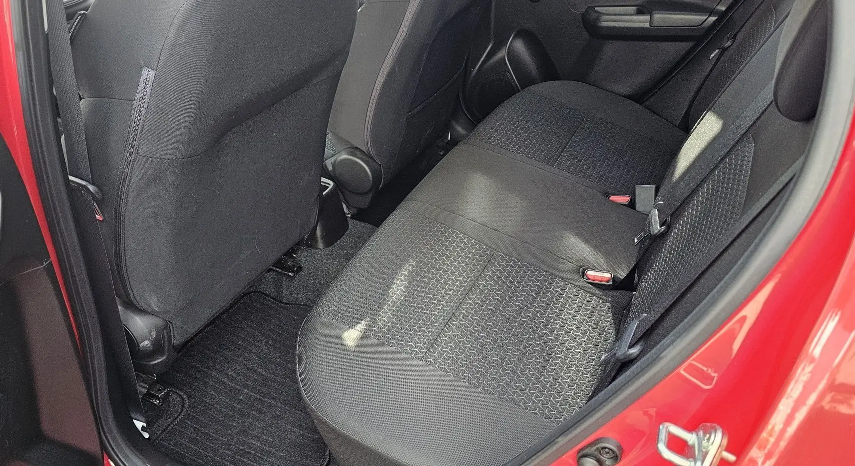 Vue intérieure côté arrière droit montrant la banquette arrière noire et la portière rouge vif d'une Suzuki Swift 2023.