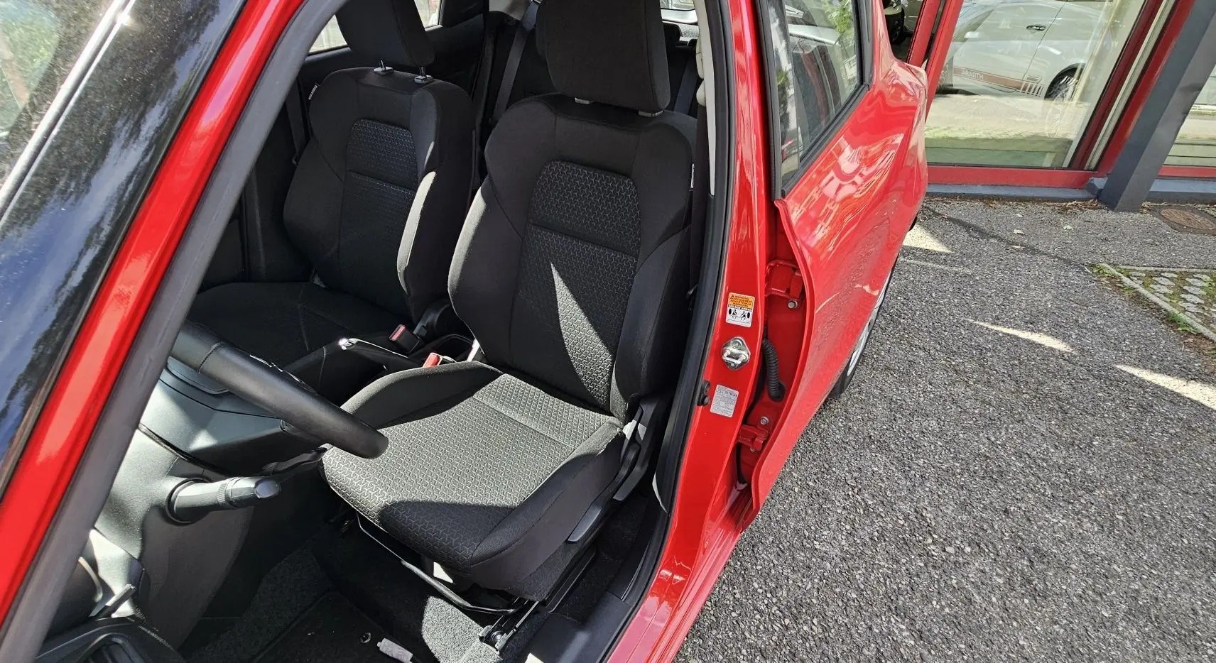 Vue intérieure côté conducteur de la Suzuki Swift 2023 rouge fervent, mettant en valeur les sièges noirs en tissu.