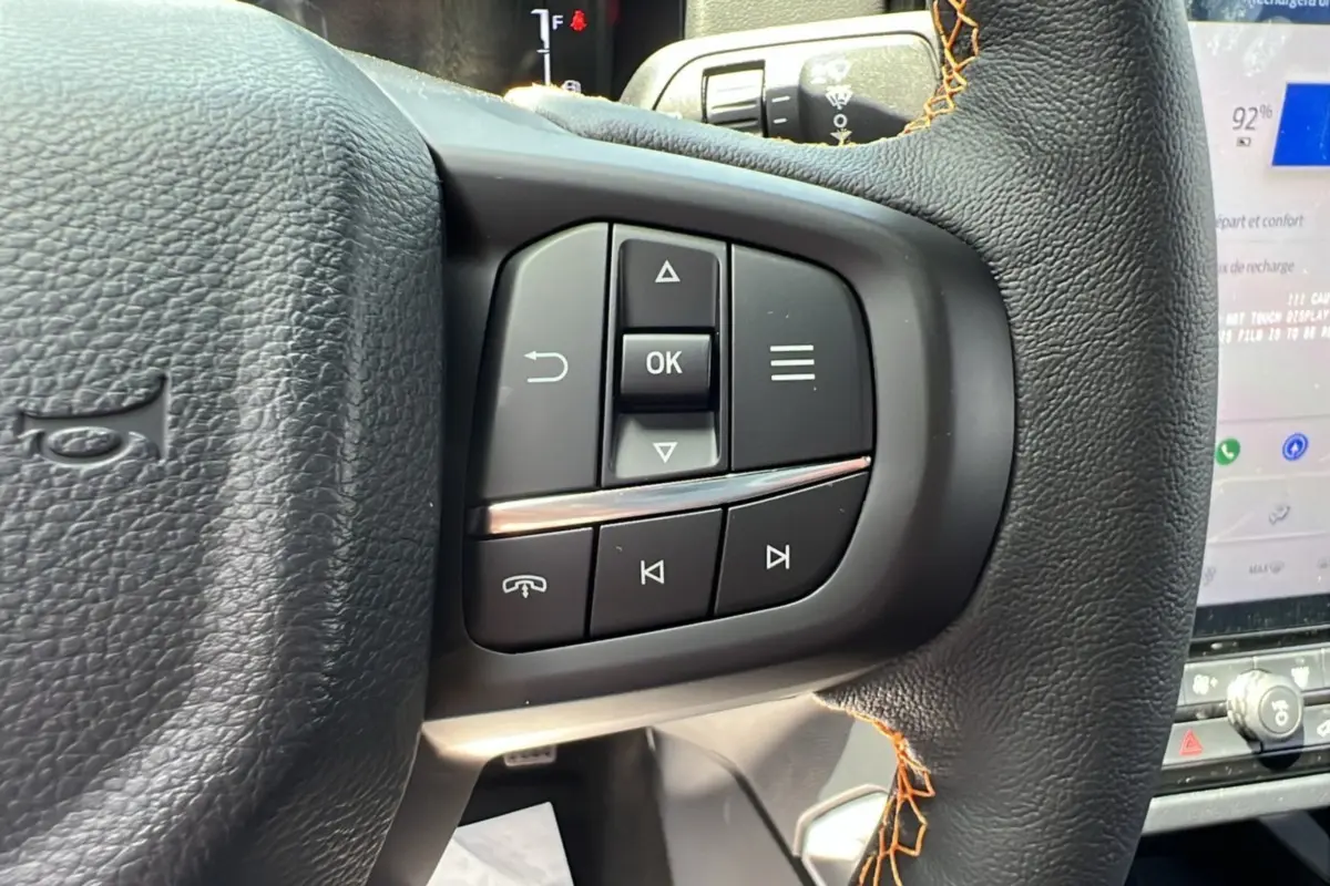 Gros plan sur les commandes au volant du Ford Ranger 2.3 PHEV Wildtrak Plus 2025 en cuir noir avec surpiqûres orange.