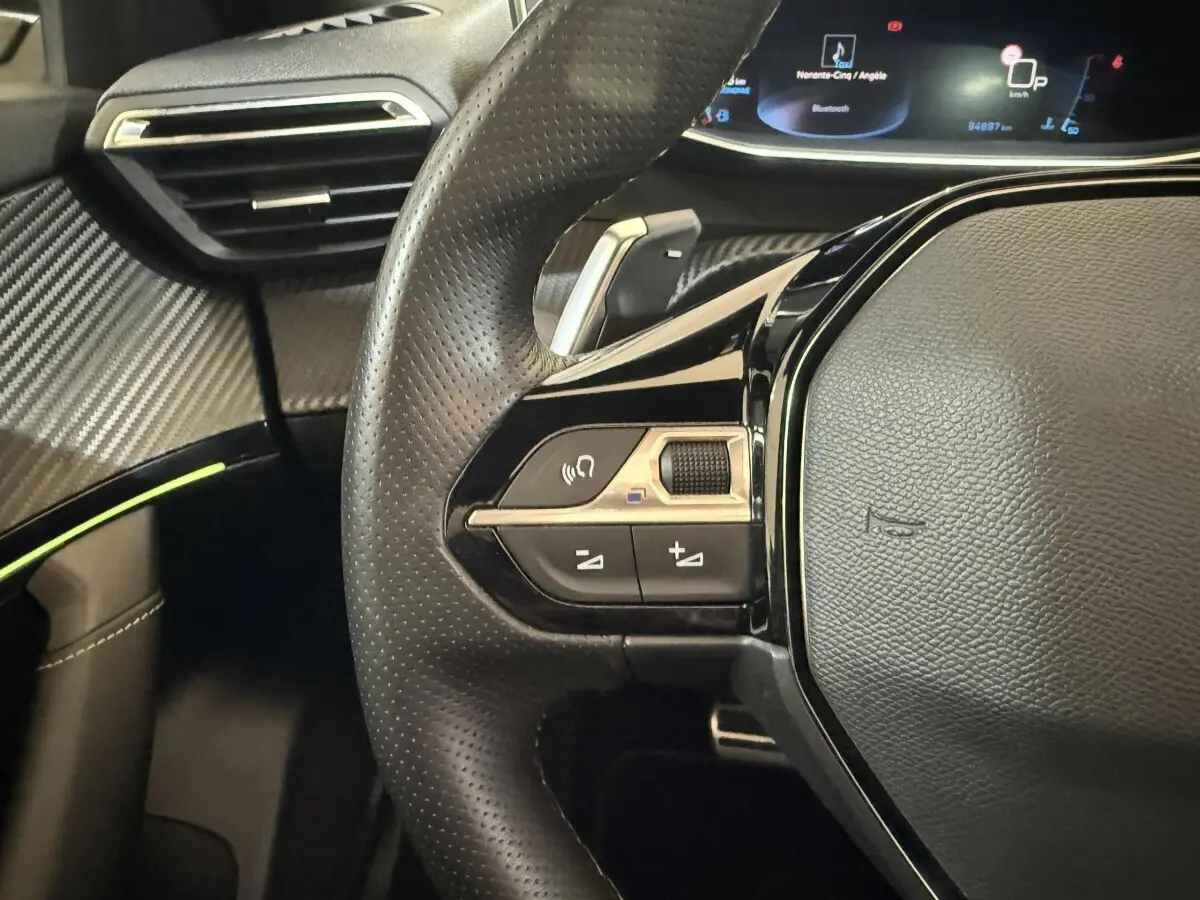 Gros plan sur le volant cuir perforé et les commandes multifonctions à gauche du Peugeot 2008 GT Pack bleu, avec tableau de bord numérique.