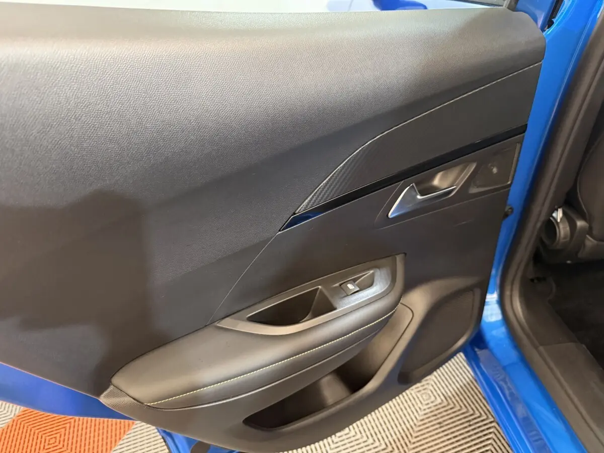 Vue rapprochée de la porte avant gauche intérieure du Peugeot 2008 bleu, avec garniture noire et bouton de fenêtre électrique.