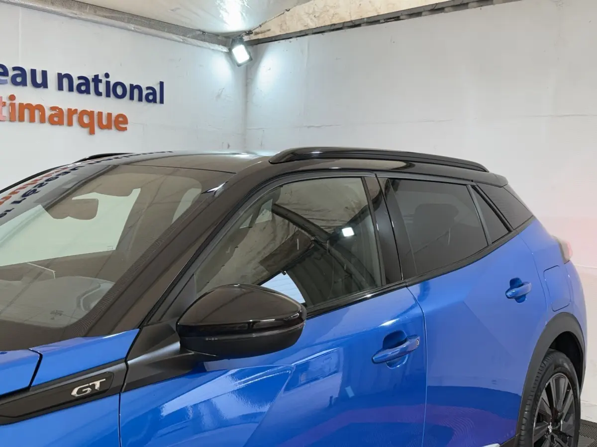 Vue côté gauche avant d'un Peugeot 2008 GT Pack bleu avec toit noir et rétroviseur noir brillant.