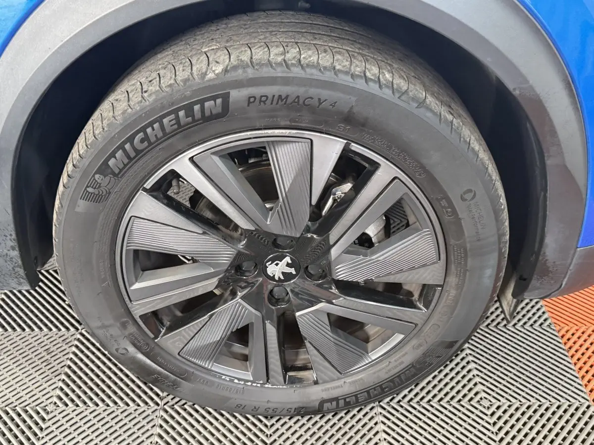 Gros plan sur la roue avant droite bleu d’un Peugeot 2008 avec jante alliage noire et grise distinctive.