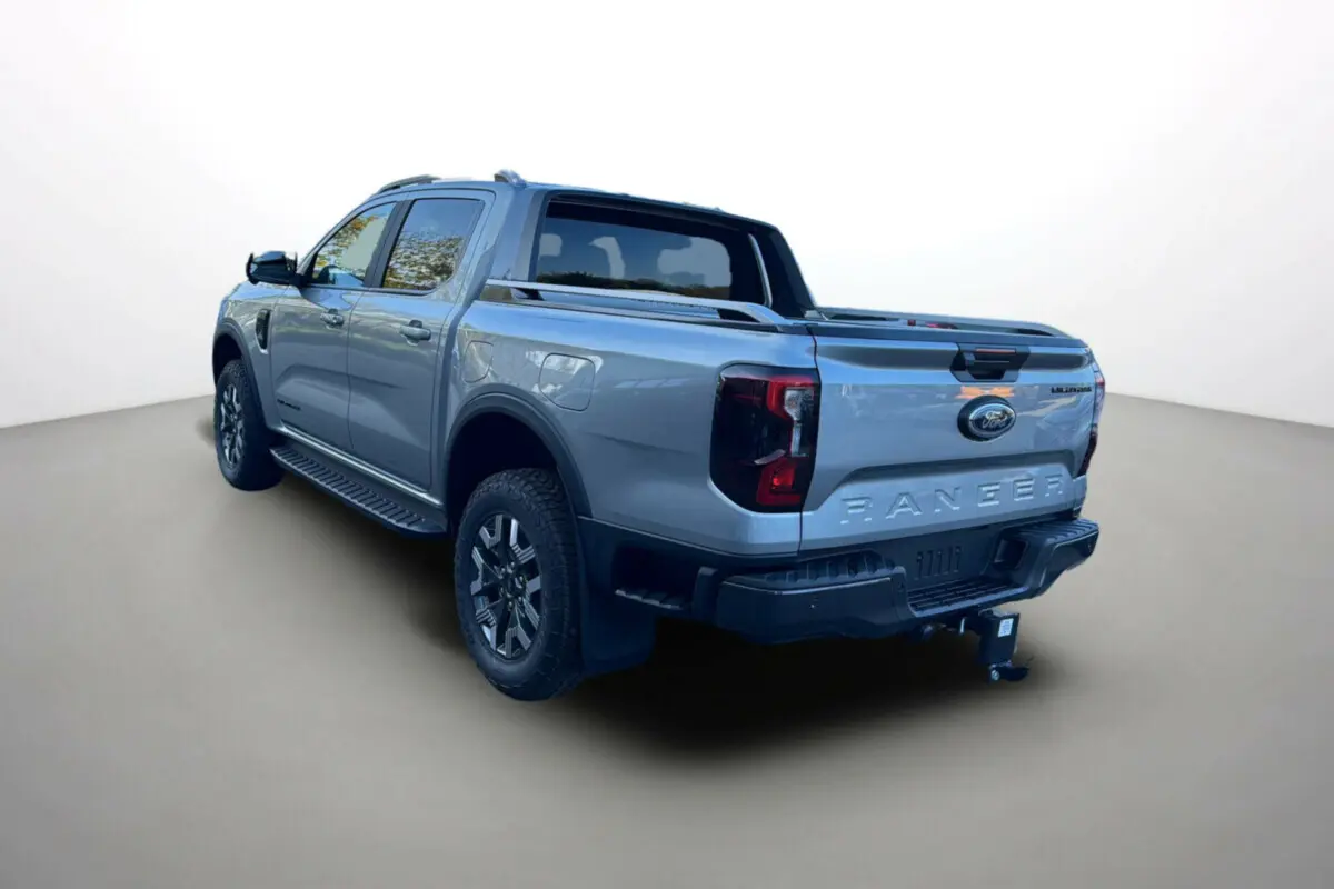 Ford Ranger PHEV gris iconic vu en 3/4 arrière droit avec attelage et barres de toit visibles.