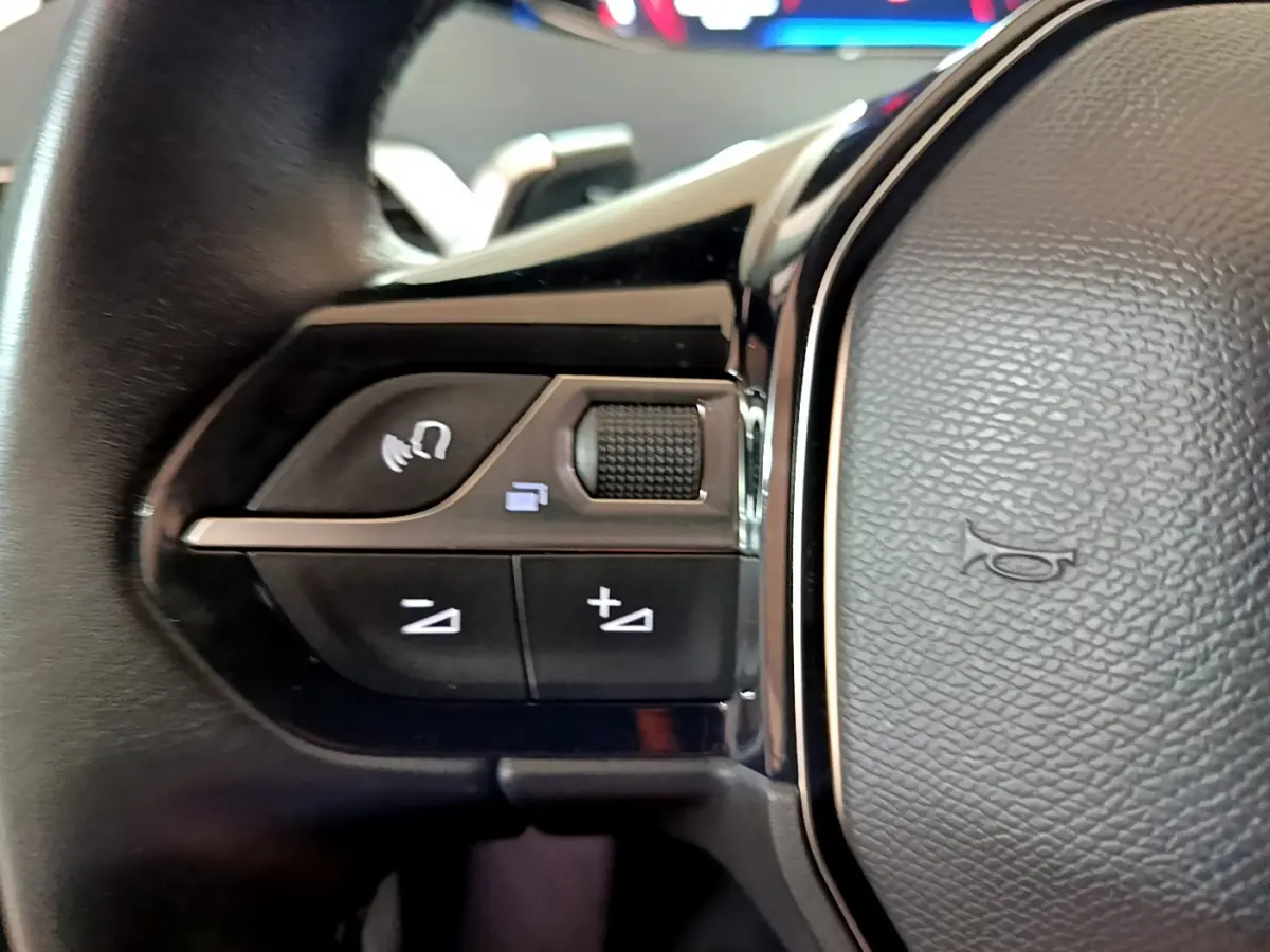 Gros plan sur les commandes gauche du volant cuir du Peugeot 5008 gris clair, avec boutons de volume et téléphone.