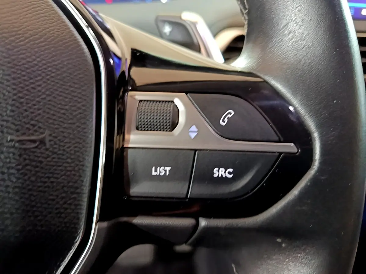 Gros plan sur les commandes gauche du volant cuir noir du Peugeot 5008 gris clair, boutons appel et liste audio visibles.