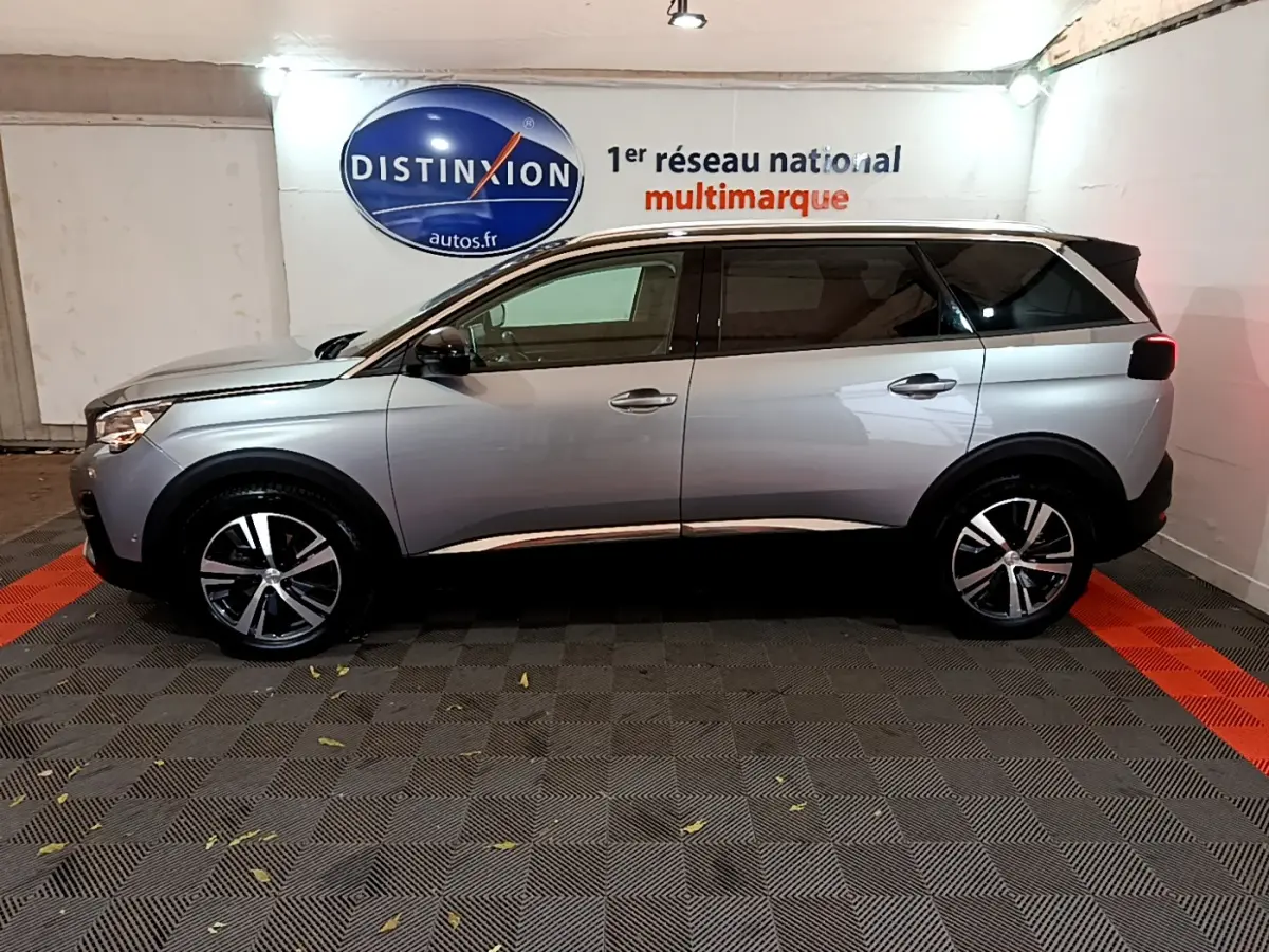 Profil côté gauche d’un Peugeot 5008 gris clair 2020 garé en intérieur avec jantes alliage et vitres teintées.