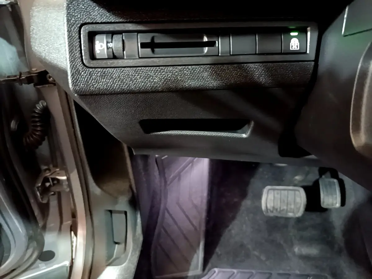 Vue du côté gauche intérieur du Peugeot 5008 gris clair 2020, montrant les pédales et commandes sous le tableau de bord.