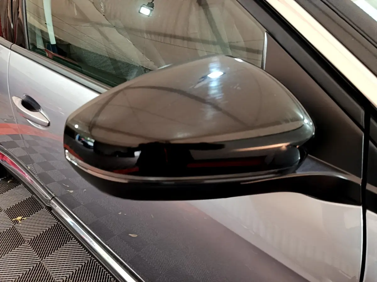 Rétroviseur noir brillant côté conducteur d’un Peugeot 5008 gris clair vu de près en intérieur.