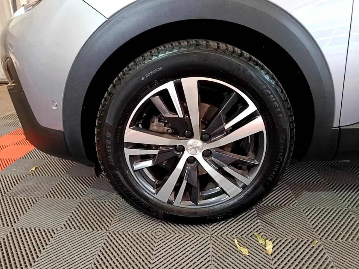 Gros plan sur la roue arrière droite du Peugeot 5008 gris clair, avec jante alliage bicolore et logo Peugeot central.