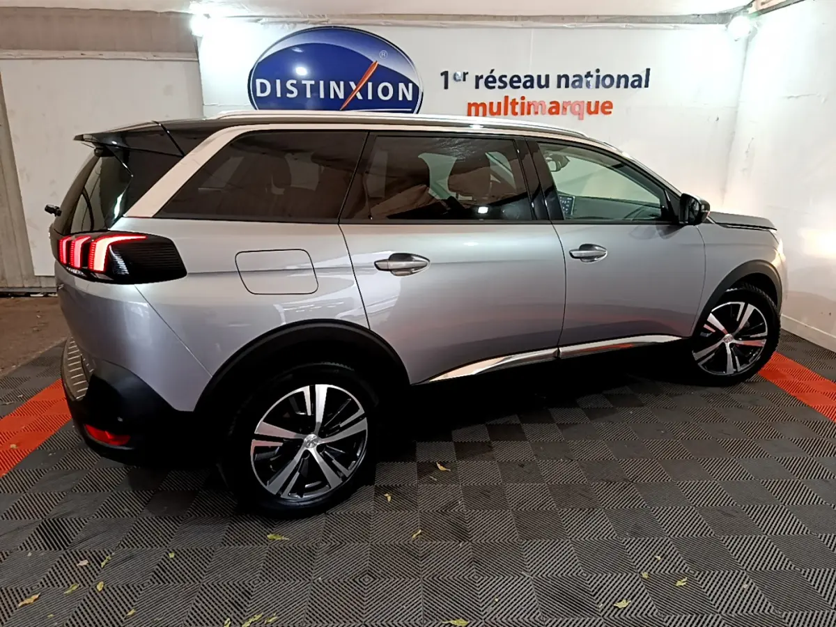 Peugeot 5008 gris clair vue de profil côté gauche, avec feux arrière allumés et jantes alliage modernes.
