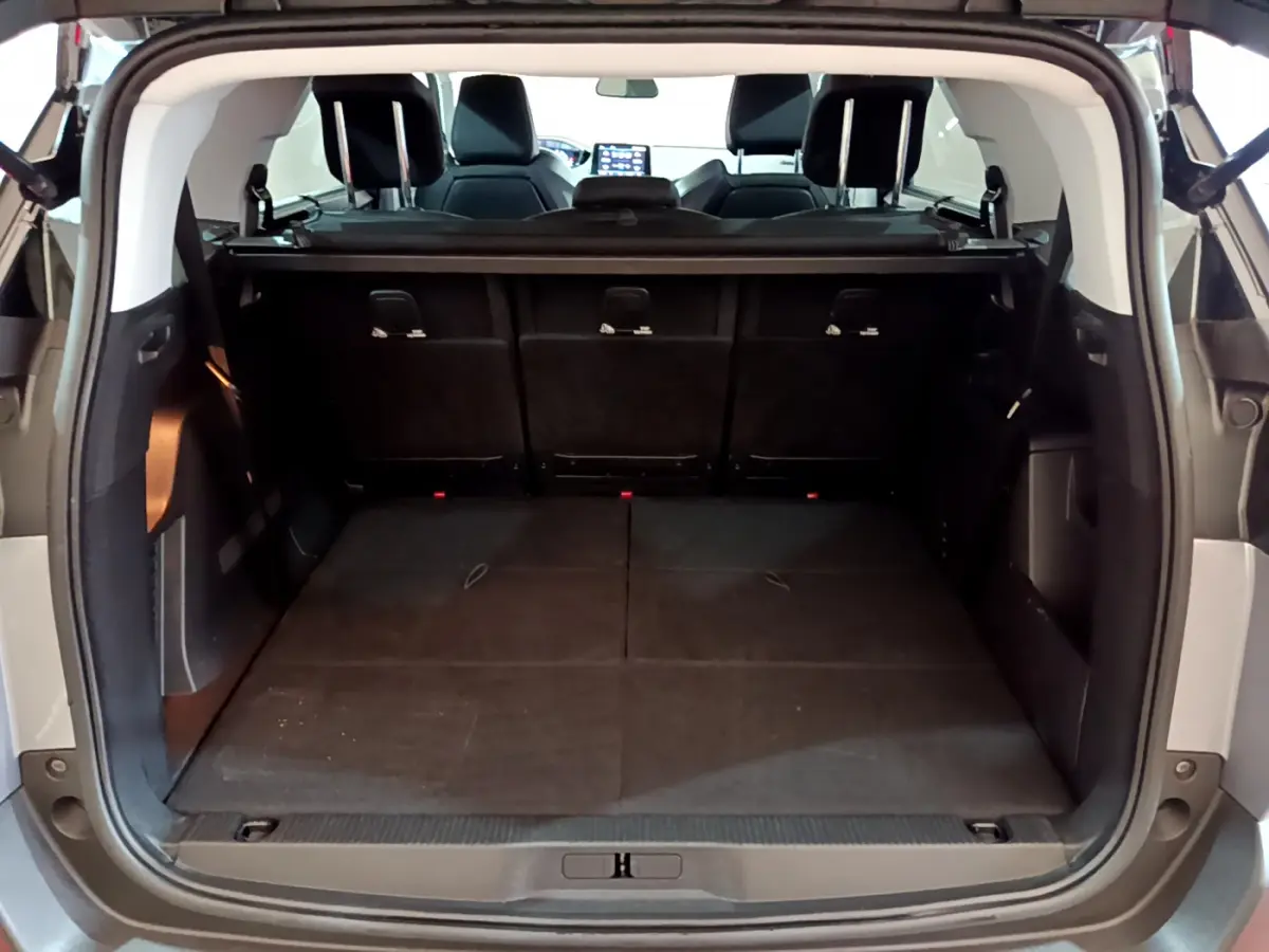 Coffre spacieux ouvert vu de l'arrière d'un Peugeot 5008 gris clair, avec sièges arrière relevés et tablette de coffre.