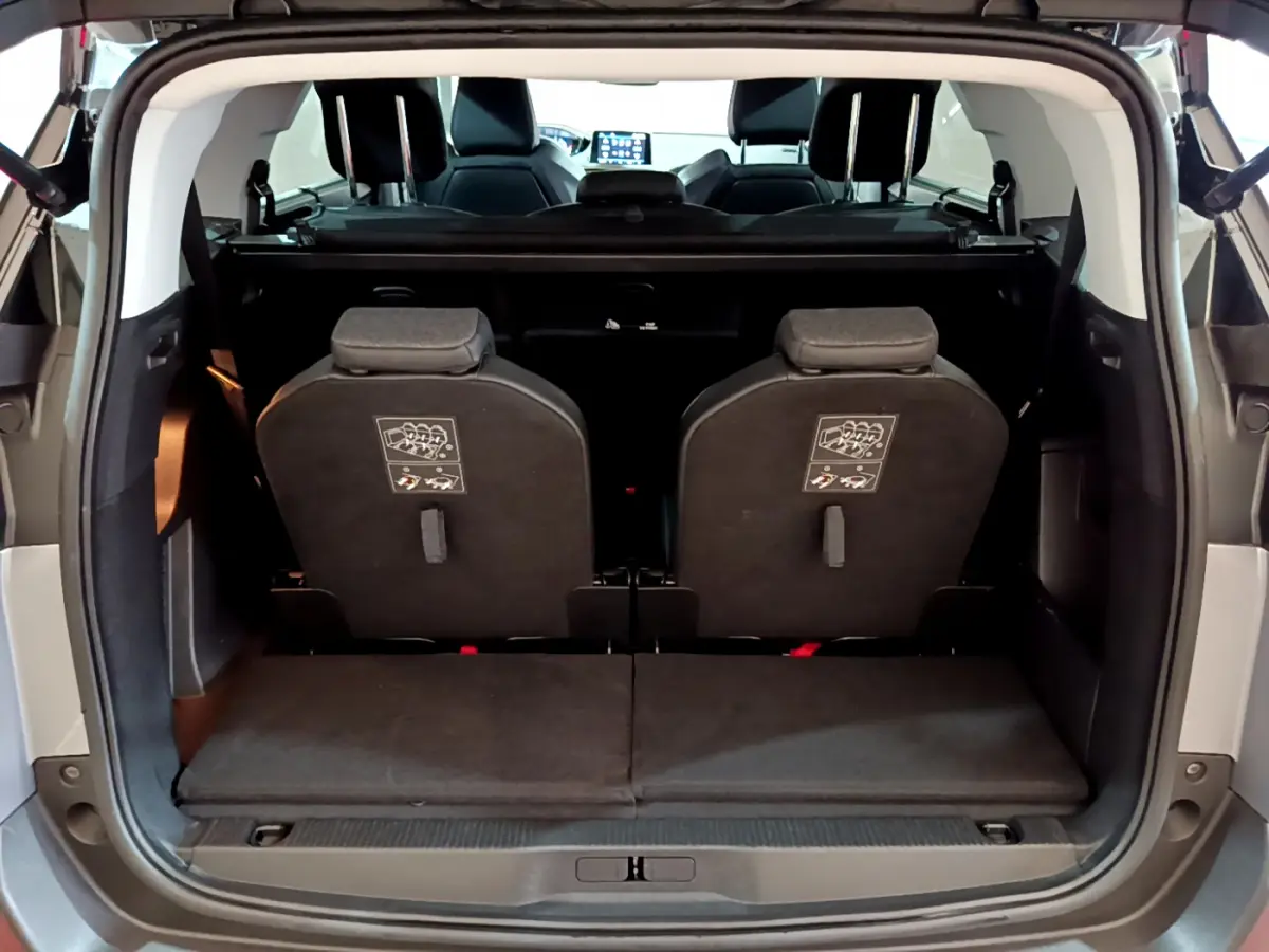 Vue arrière du coffre ouvert d'un Peugeot 5008 gris clair, montrant la 3ème rangée de sièges individuels relevés.