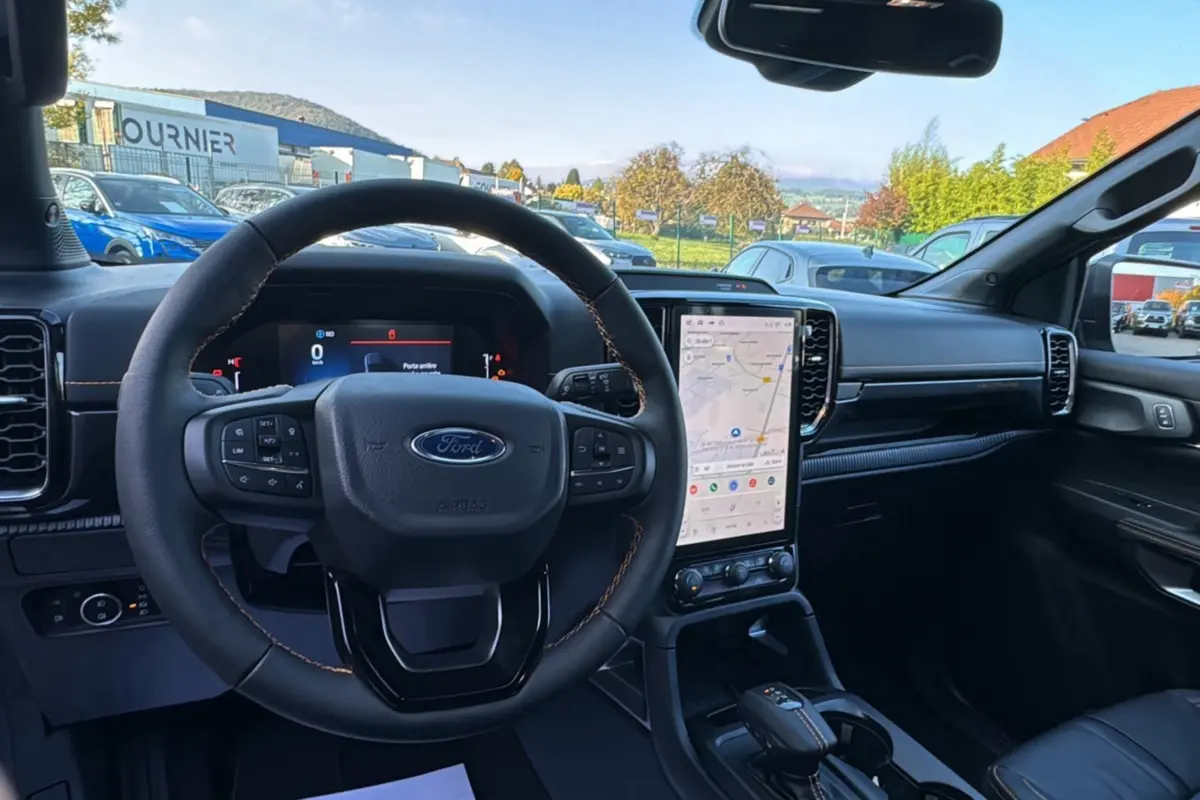 Intérieur du Ford Ranger PHEV 2025 vu du siège conducteur, volant cuir, écran tactile vertical avec navigation affichée.