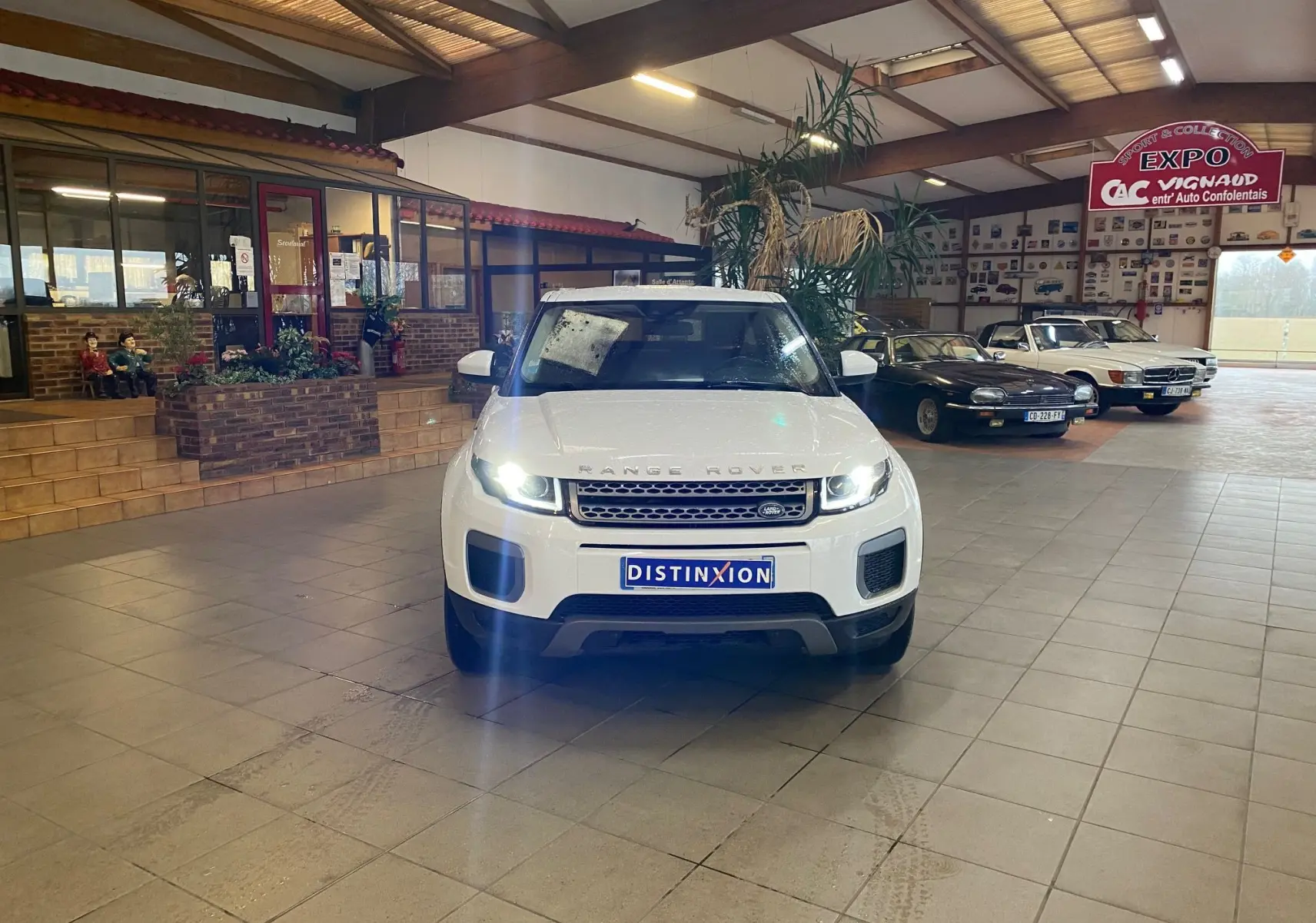 Vue avant d'un Range Rover Evoque blanc 2016 avec phares allumés dans un showroom intérieur.