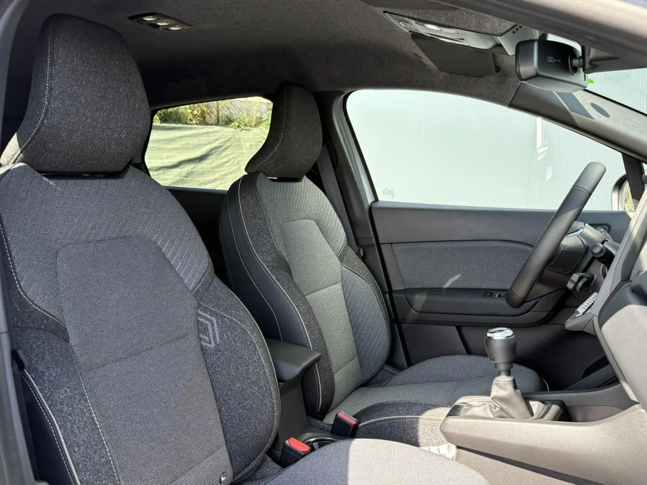 Intérieur du Renault Captur 2025 vu côté droit, sièges tissu gris avec volant et levier de vitesses manuelle visibles.