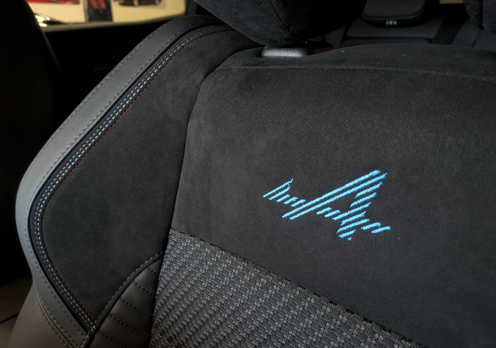Gros plan sur le siège avant en tissu et alcantara noir avec logo Alpine bleu brodé sur Renault Austral 2025.