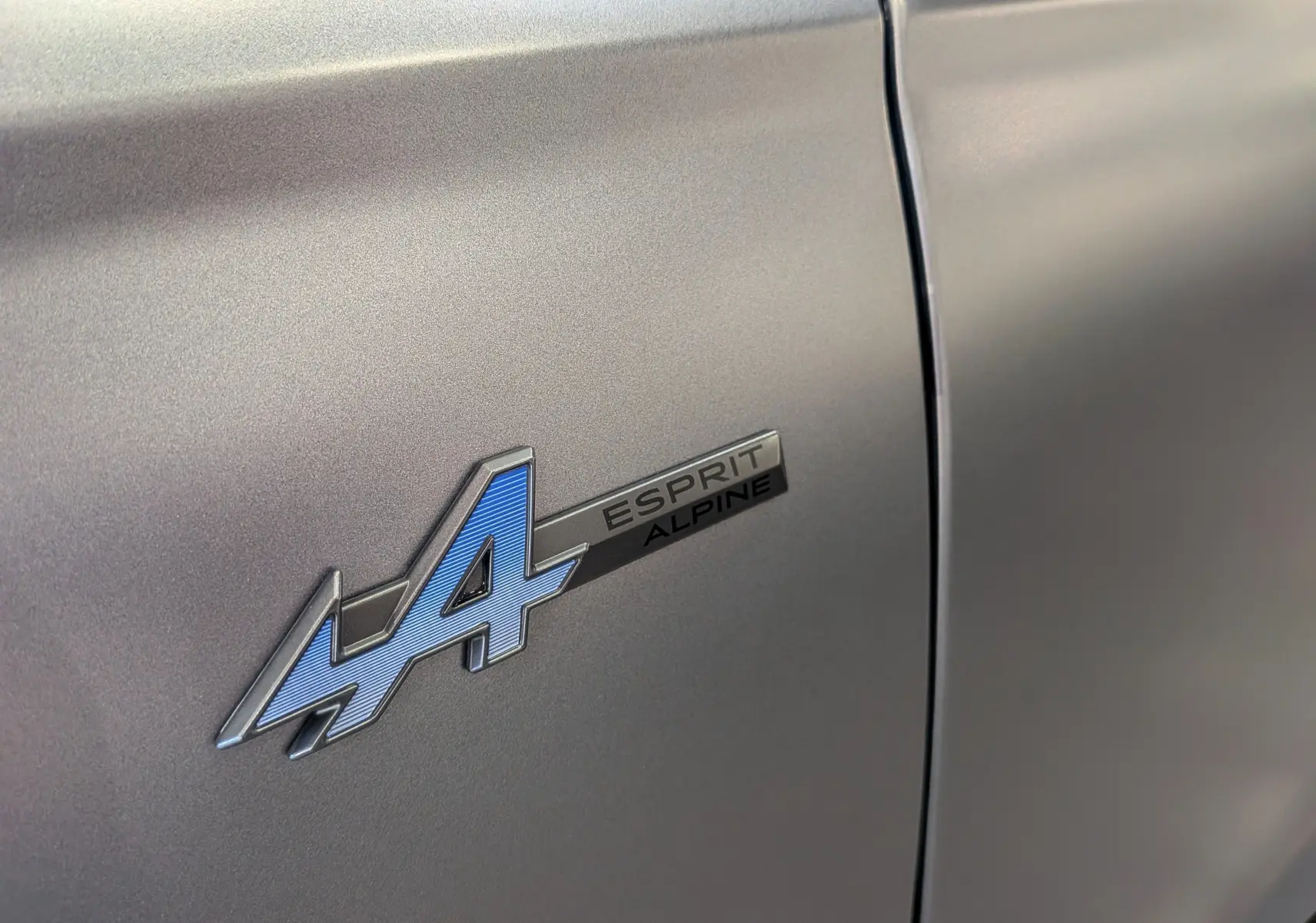 Gros plan sur l'emblème Esprit Alpine bleu sur la porte gris schiste satin du Renault Austral 2025 hybride.