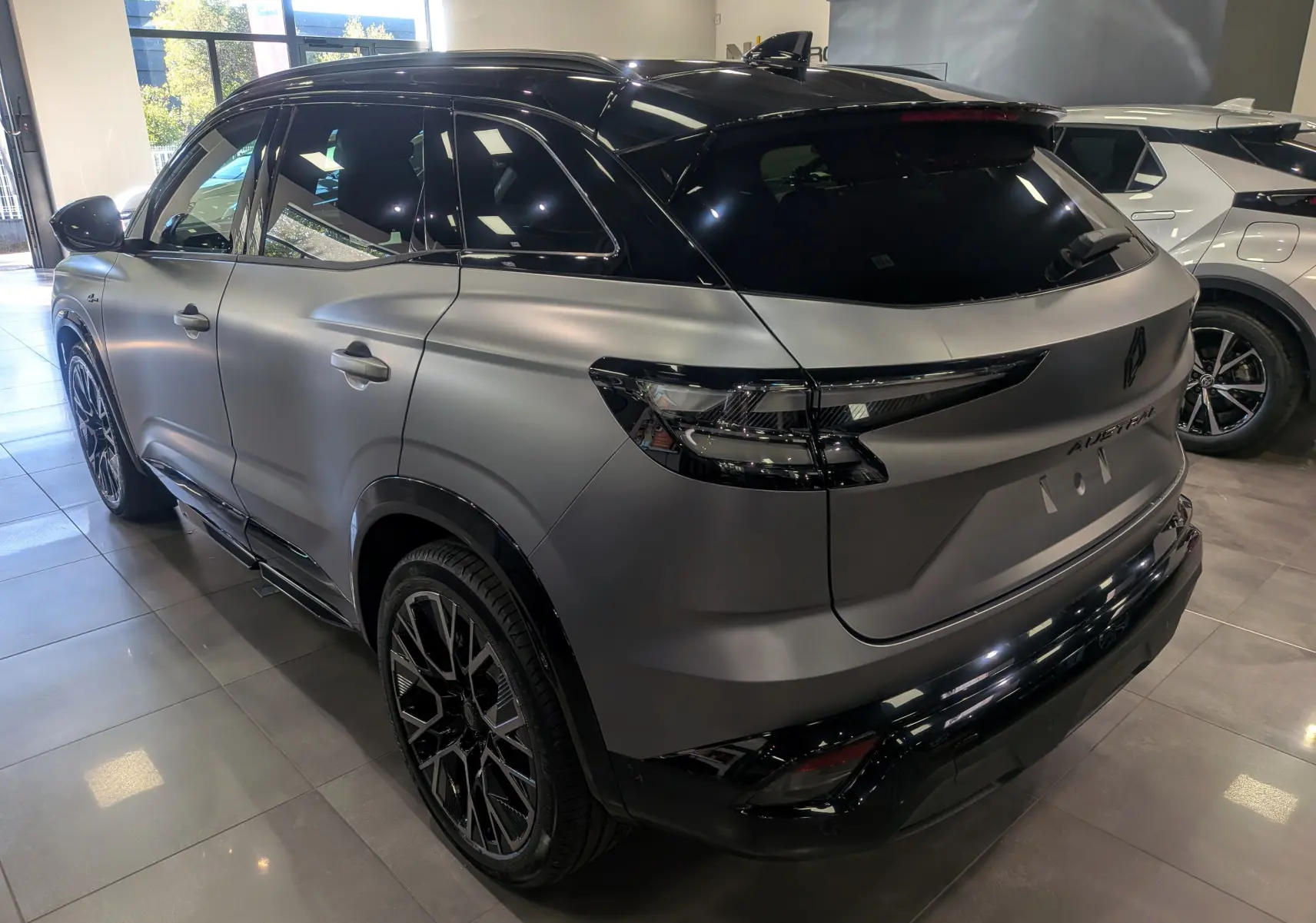 Renault Austral full hybride gris schiste satin avec toit noir, vue 3/4 arrière droit en intérieur showroom.