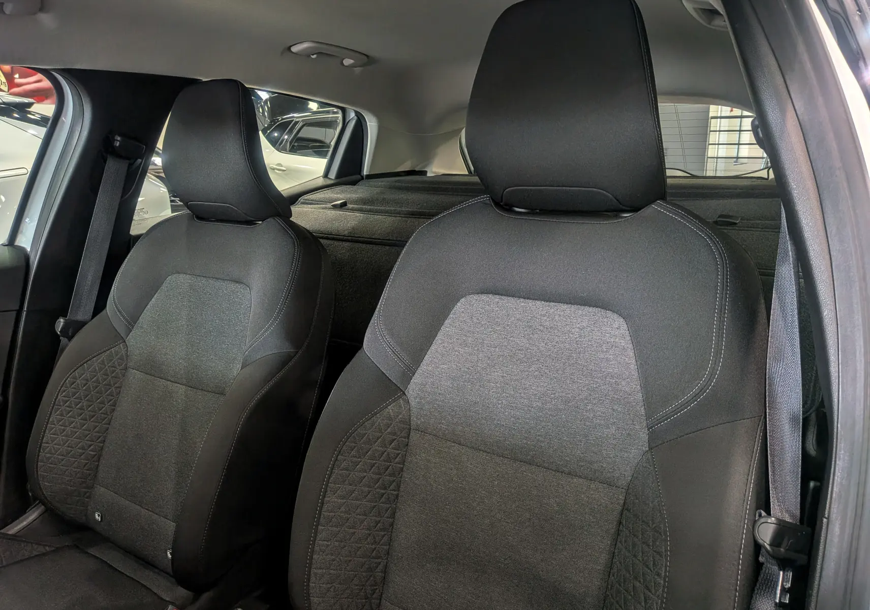 Gros plan sur les sièges avant en tissu noir et gris d'une Renault Clio V blanche, vue côté conducteur avec ceinture attachée.