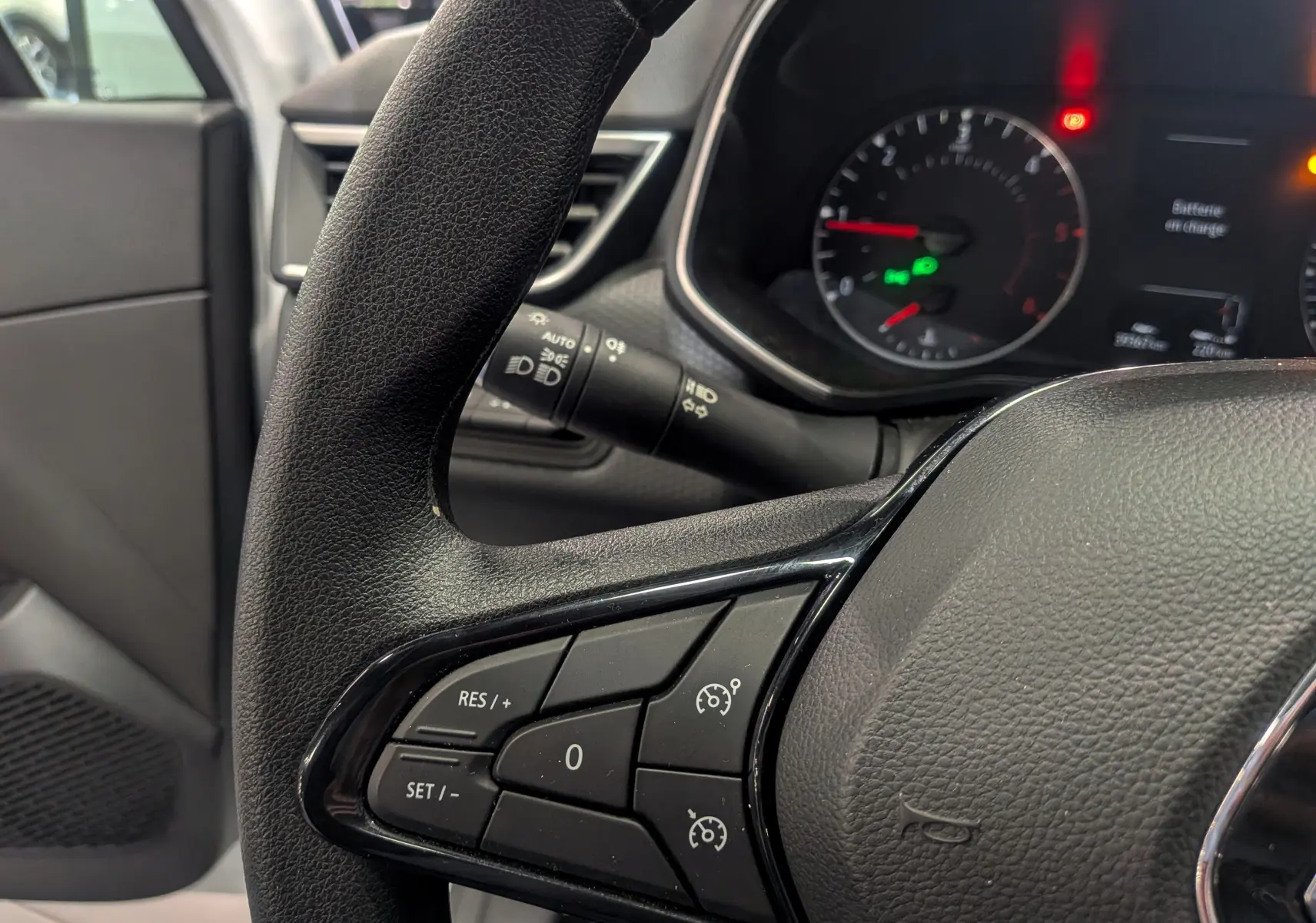 Gros plan sur le volant côté gauche de la Renault Clio V blanche, avec commandes de régulateur de vitesse visibles.