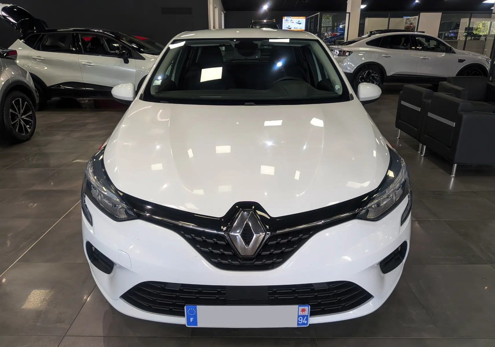 Vue frontale d'une Renault Clio V blanche Glacier en showroom, avec calandre noire et logo Renault bien visible.
