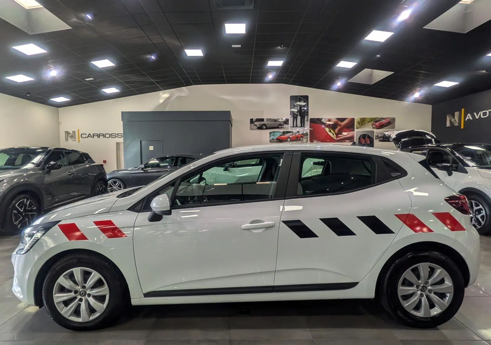 Profil droit d'une Renault Clio V blanche Glacier avec bandes rouges et noires diagonales sur les ailes avant et arrière.
