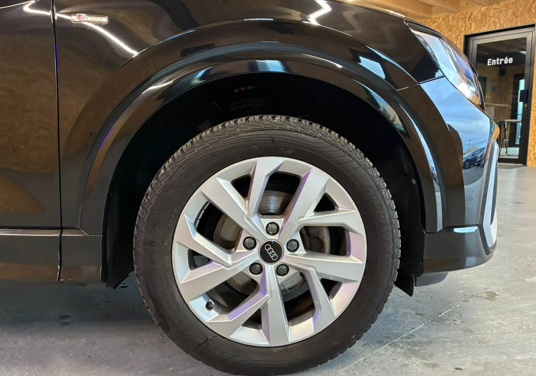 Gros plan sur la roue avant droite d'un Audi Q2 noir 2023 avec jante argentée et badge S-Line sur l'aile.
