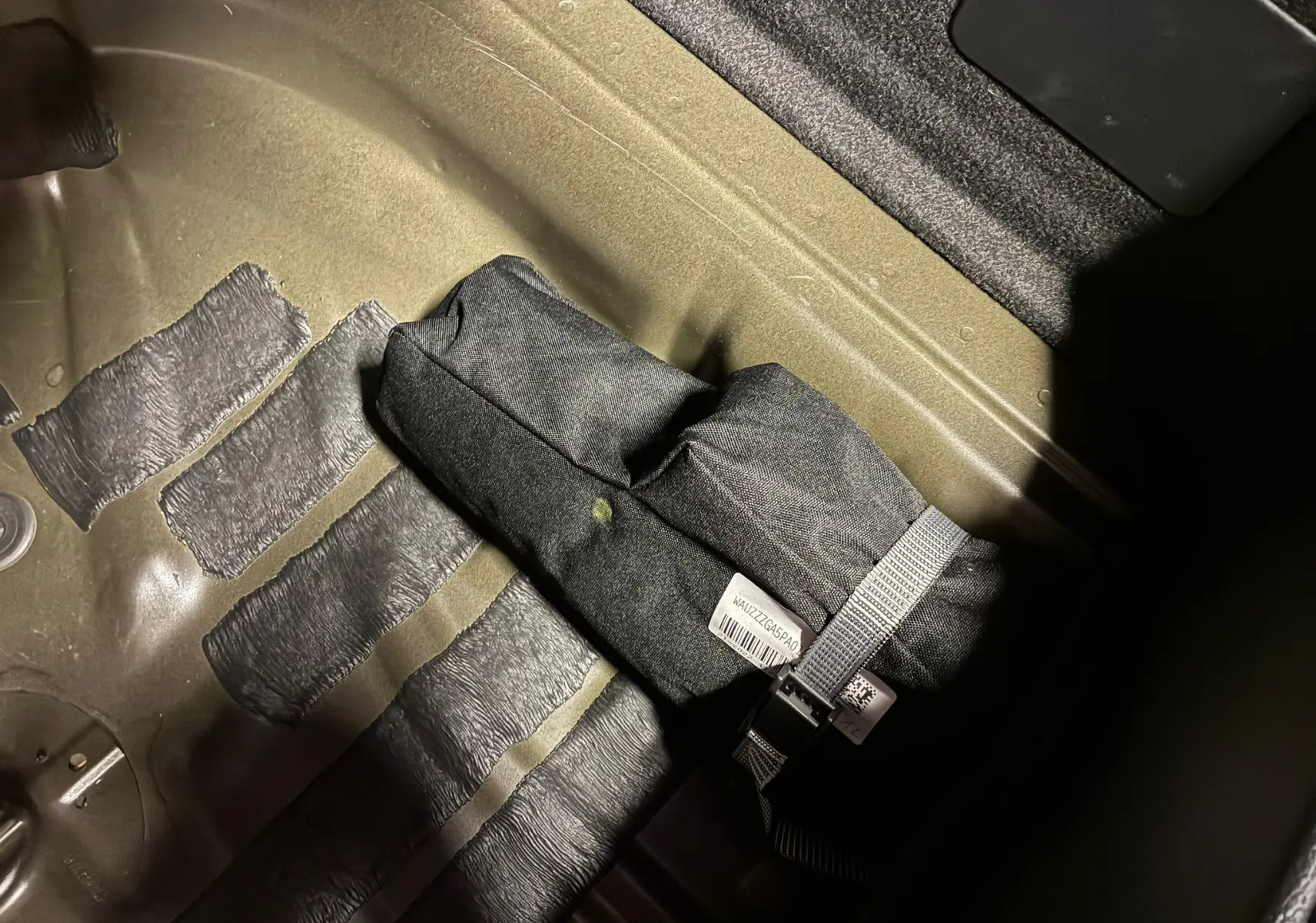 Gros plan sur un kit de secours noir fixé dans le coffre d'un Audi Q2 noir, sous un éclairage tamisé.