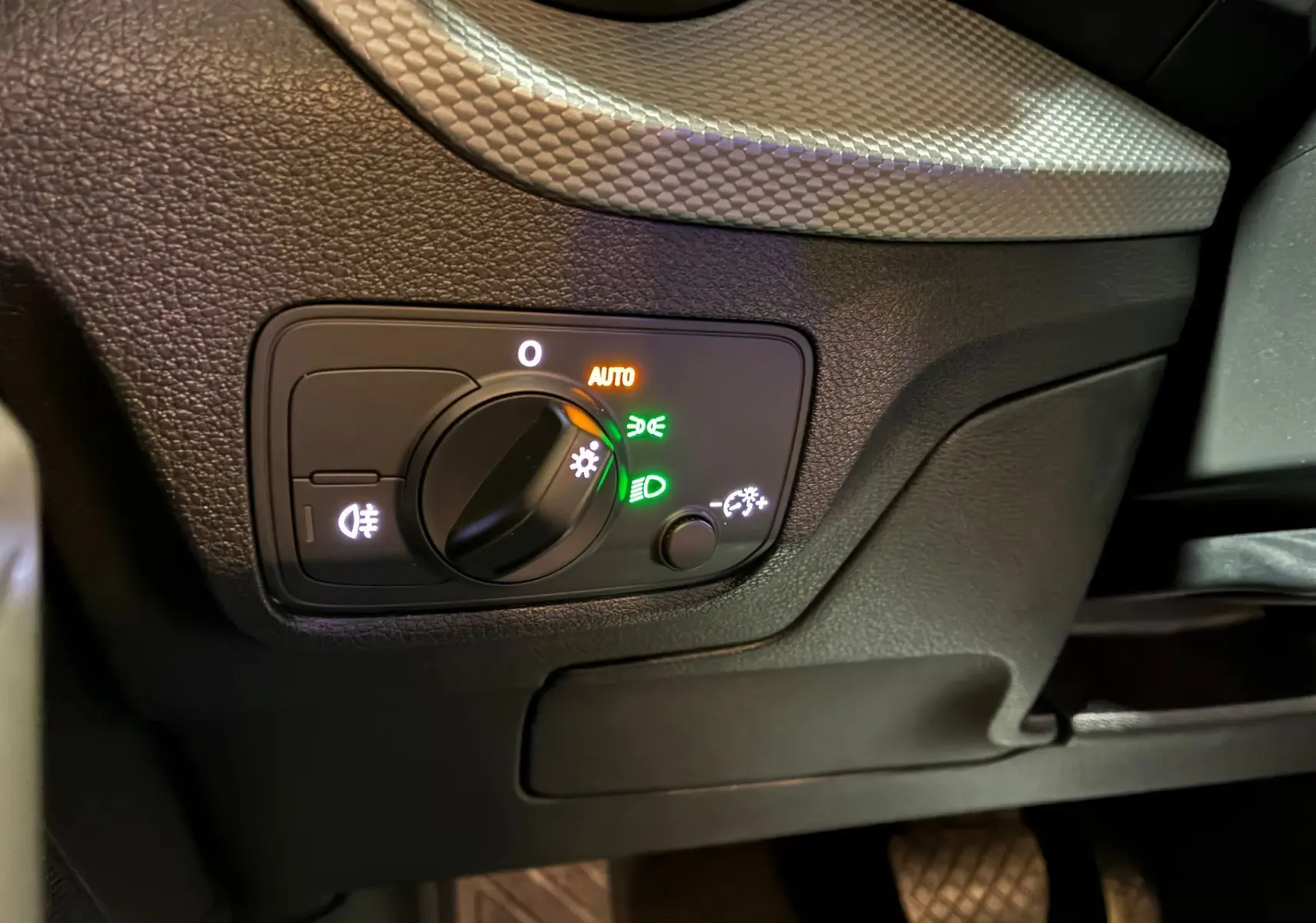 Gros plan sur le bouton de commande des phares avec éclairage automatique dans l'habitacle noir de l'Audi Q2 2023.
