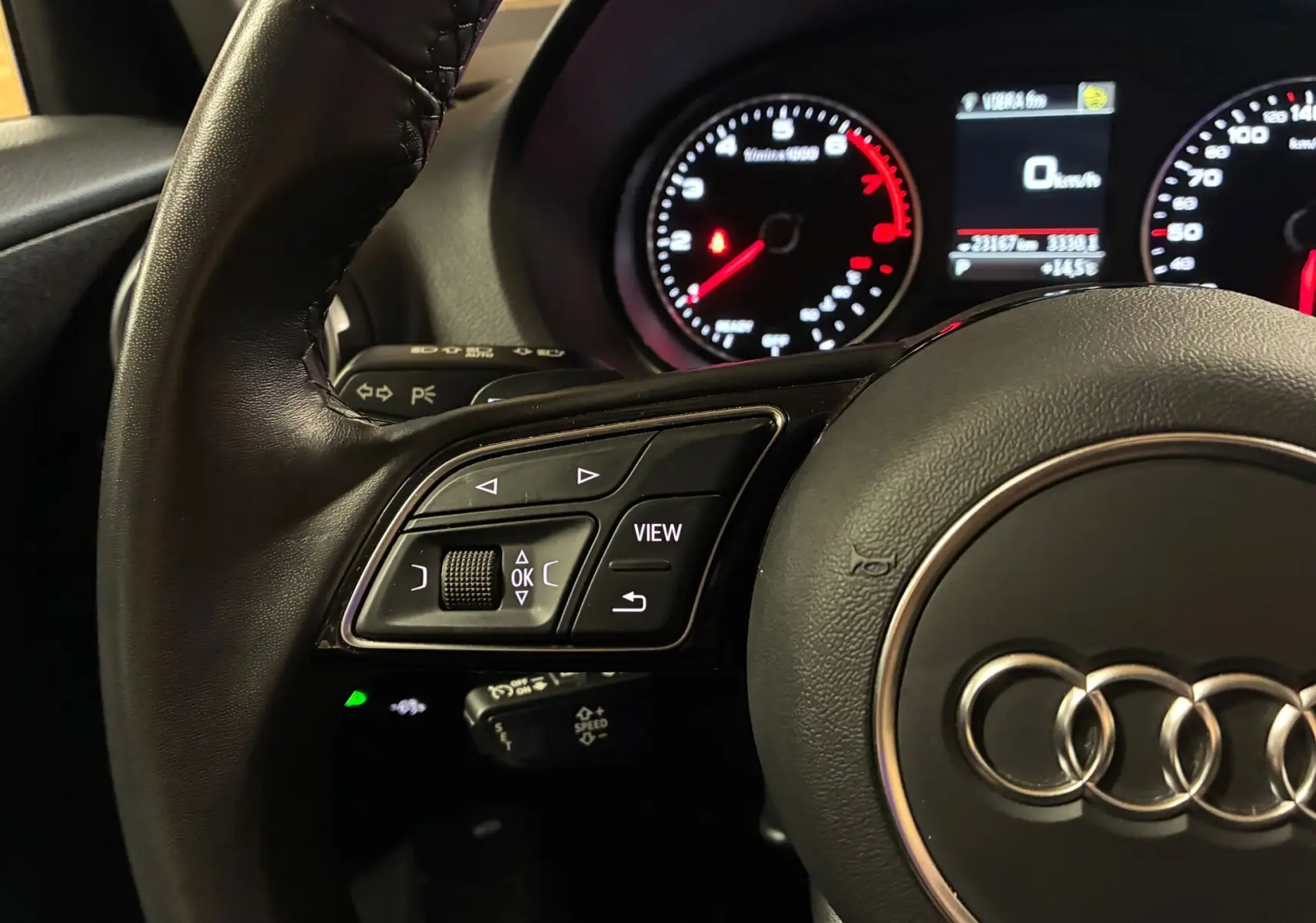 Gros plan sur le volant noir de l'Audi Q2 35 TFSI S-Line avec commandes intégrées et tableau de bord éclairé en arrière-plan.