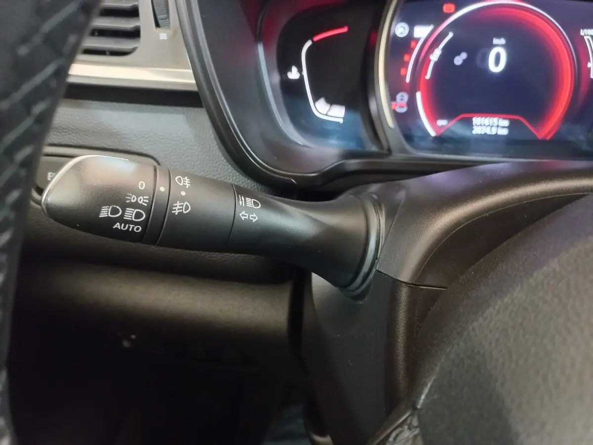 Gros plan sur la manette des phares et clignotants à gauche du volant du Renault Kadjar gris foncé, tableau de bord numérique en arrière-plan.