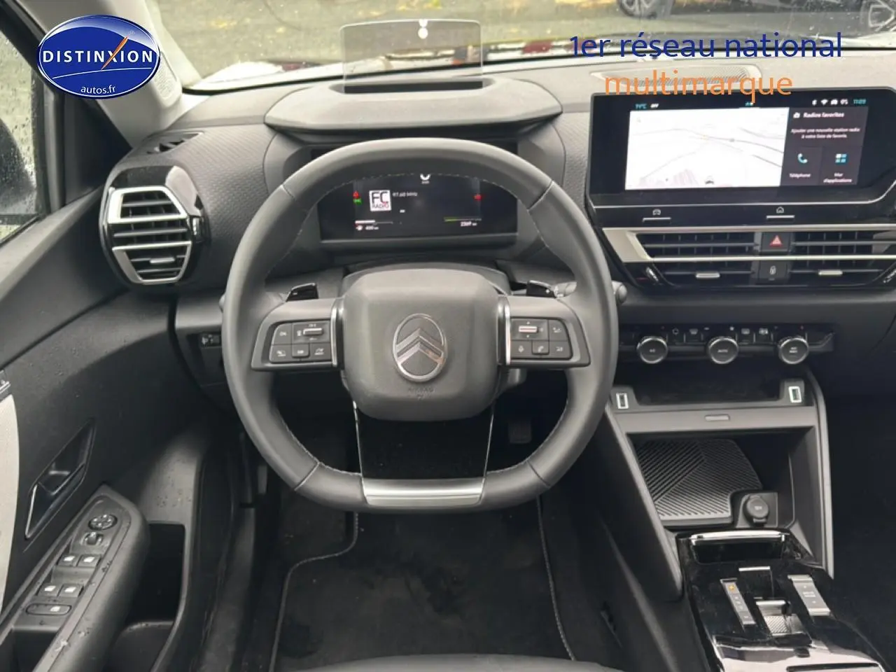Vue intérieure frontale du poste de conduite noir de la Citroën C4 1.2 hybride 2025 avec écran tactile et volant multifonctions.