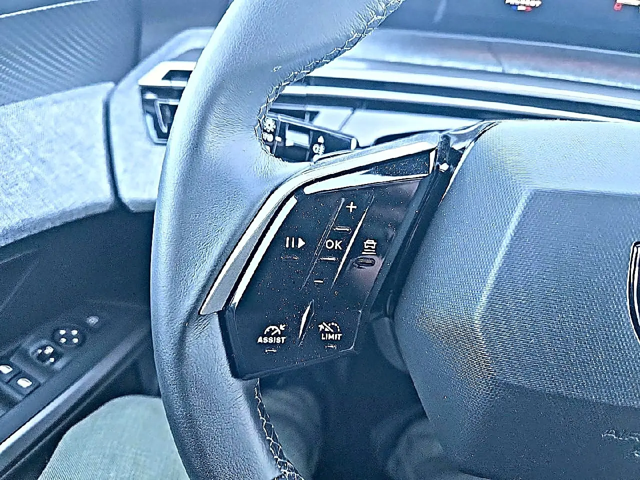 Gros plan sur le volant cuir noir du Peugeot 5008 Hybrid 145 allure, avec commandes multifonctions visibles côté gauche.