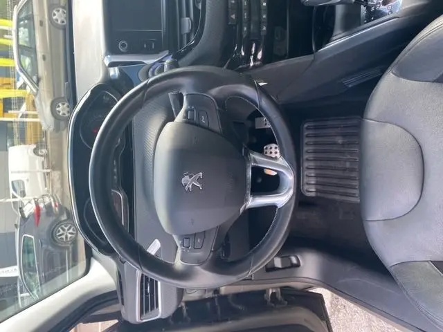 Vue intérieure centrée sur le volant Peugeot d'une 208 gris mat 2015, avec siège conducteur et pédalier visibles.