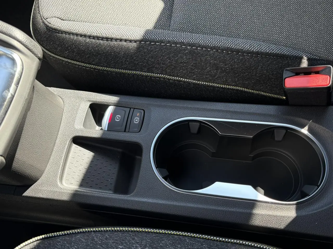 Gros plan sur la console centrale noire du Renault Captur blanc nacré 2025 avec porte-gobelets et commandes de frein à main électrique.