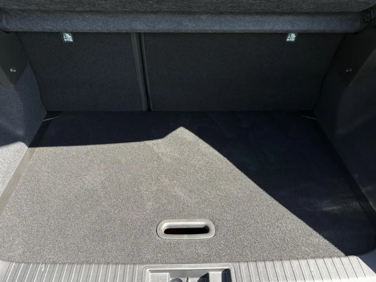 Coffre spacieux du Renault Captur blanc nacré 2025 vu de l'intérieur, avec plancher de coffre mobile et tapis gris.