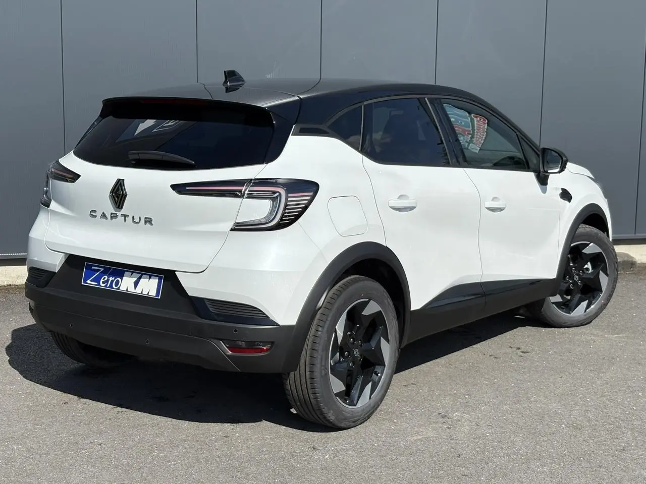 Vue 3/4 arrière droite du Renault Captur blanc nacré avec toit noir étoilé et jantes noires distinctives.