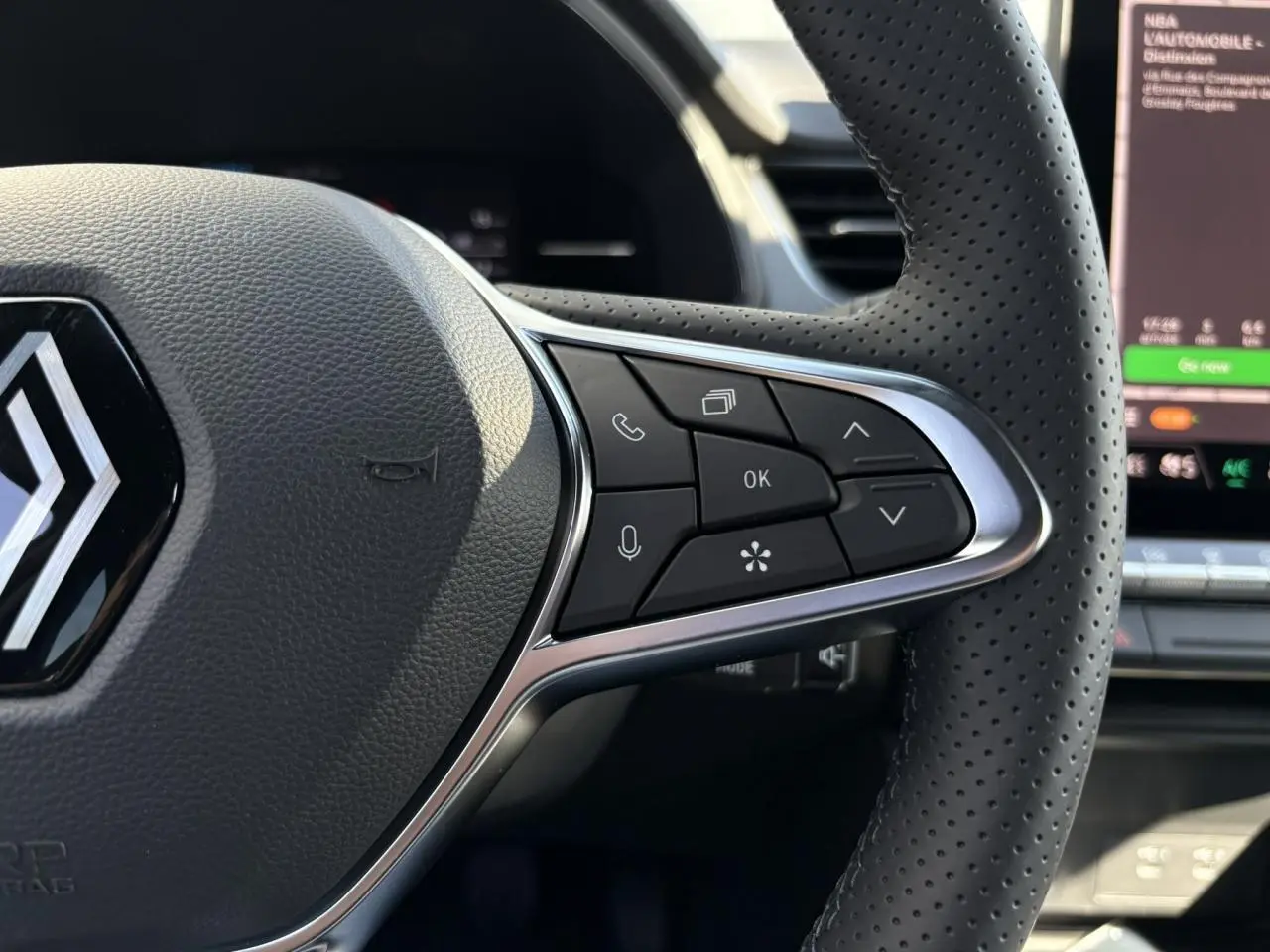 Gros plan sur le volant perforé du Renault Captur 2025 avec commandes multifonctions et logo au centre.