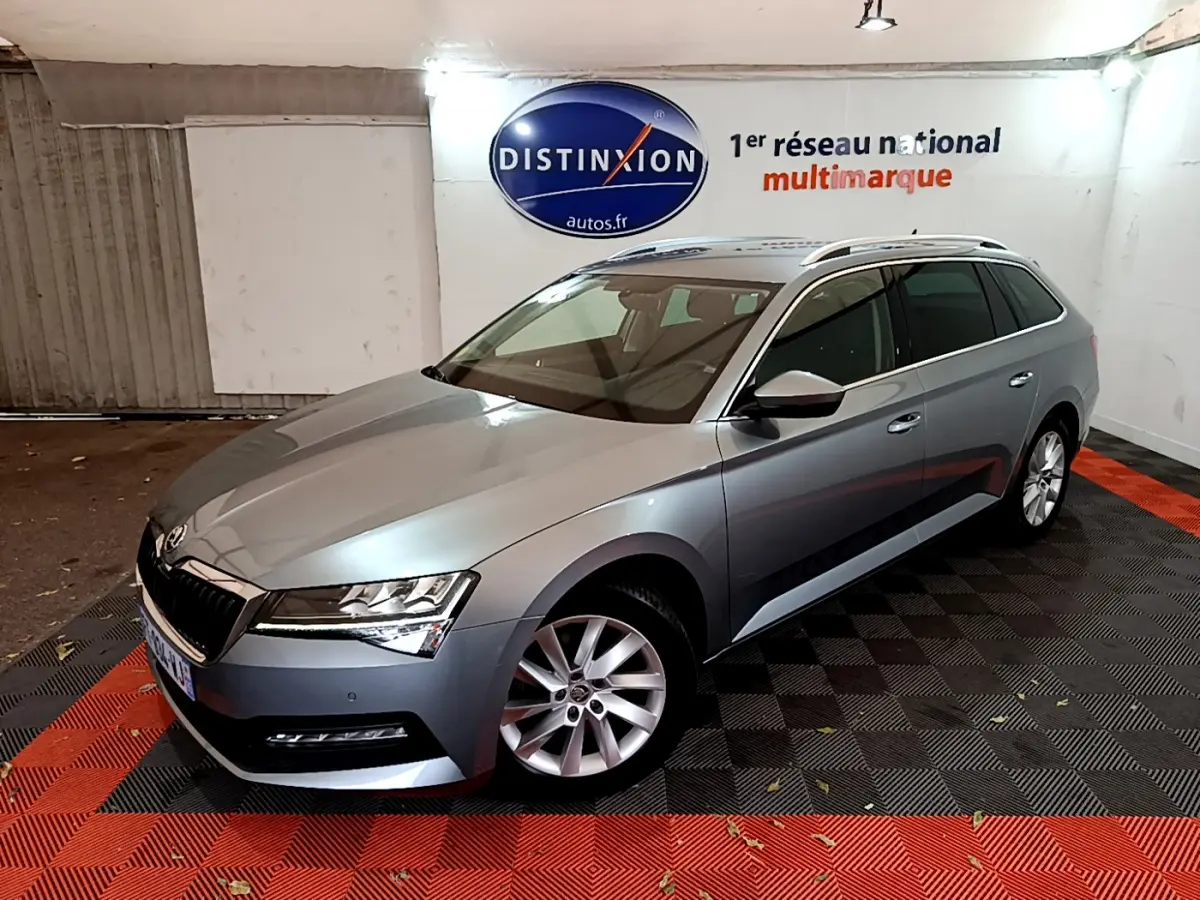 Vue 3/4 avant droite d'une Skoda Superb gris clair en break, stationnée en intérieur sur sol noir et rouge.