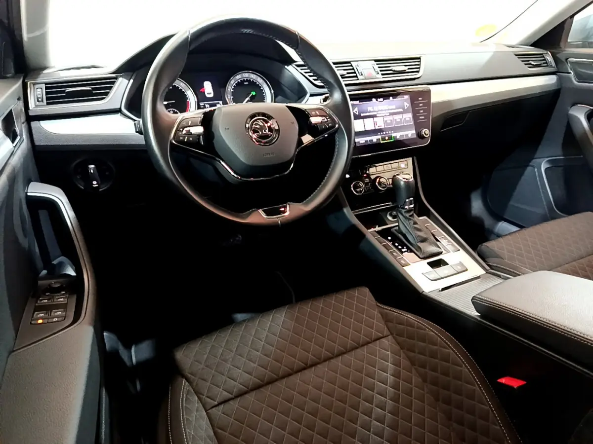 Intérieur de la Skoda Superb 2020 vu côté conducteur, volant cuir, console centrale avec écran tactile et sièges noirs matelassés.