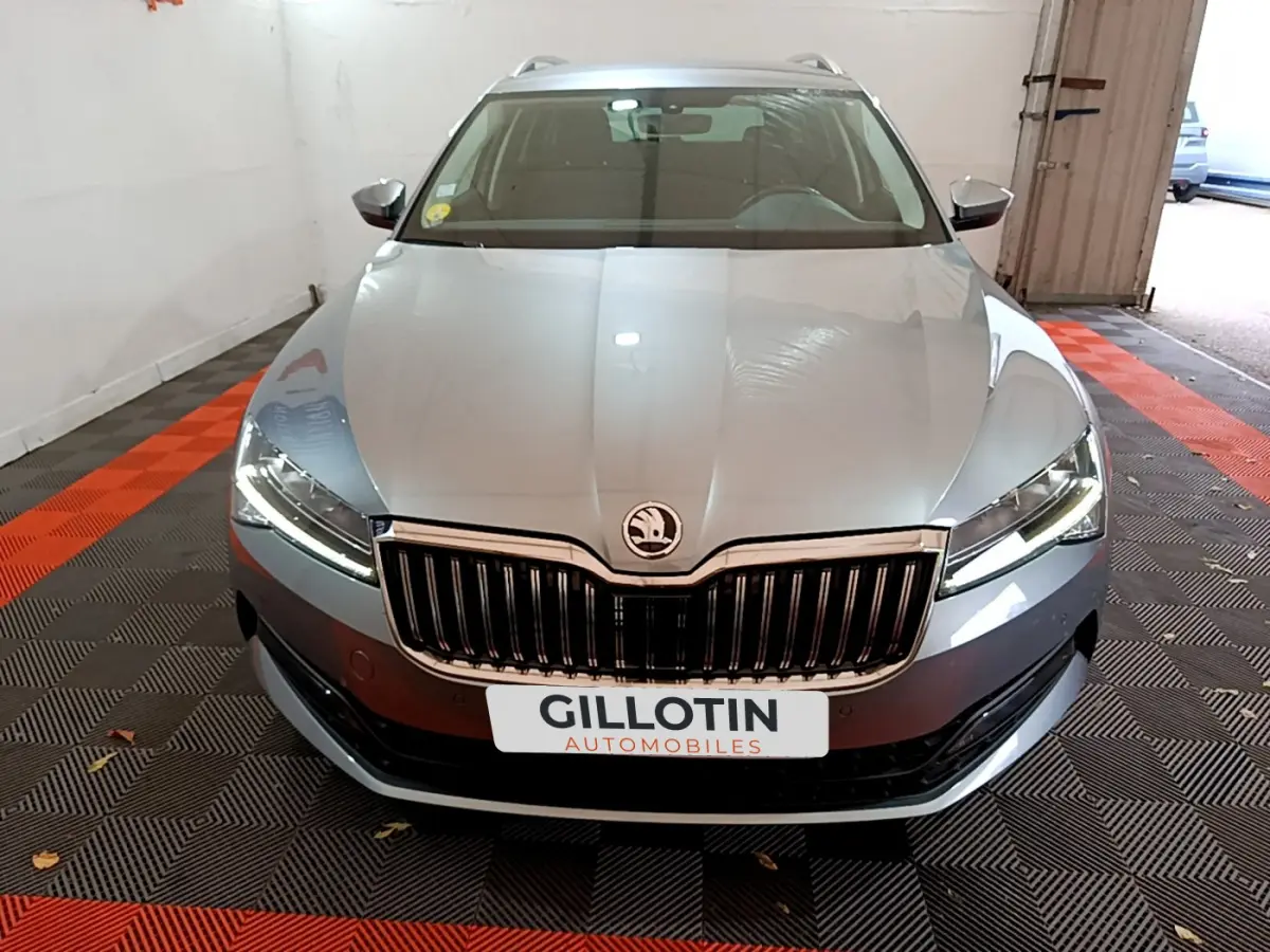 Vue frontale d'une Skoda Superb gris clair avec calandre chromée et phares LED allumés en intérieur.
