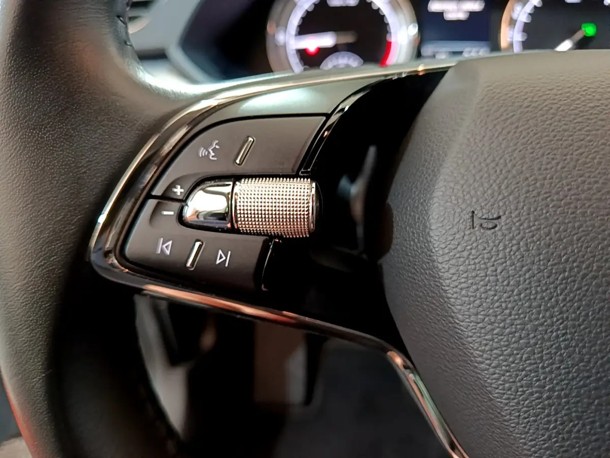 Gros plan sur la commande gauche du volant cuir d'une Skoda Superb gris clair, avec molette crantée et boutons multifonctions.