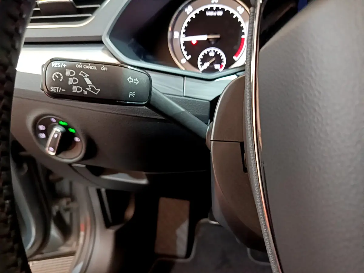 Gros plan sur la commande de régulateur de vitesse à gauche du volant cuir dans l'habitacle de la Skoda Superb gris clair 2020.