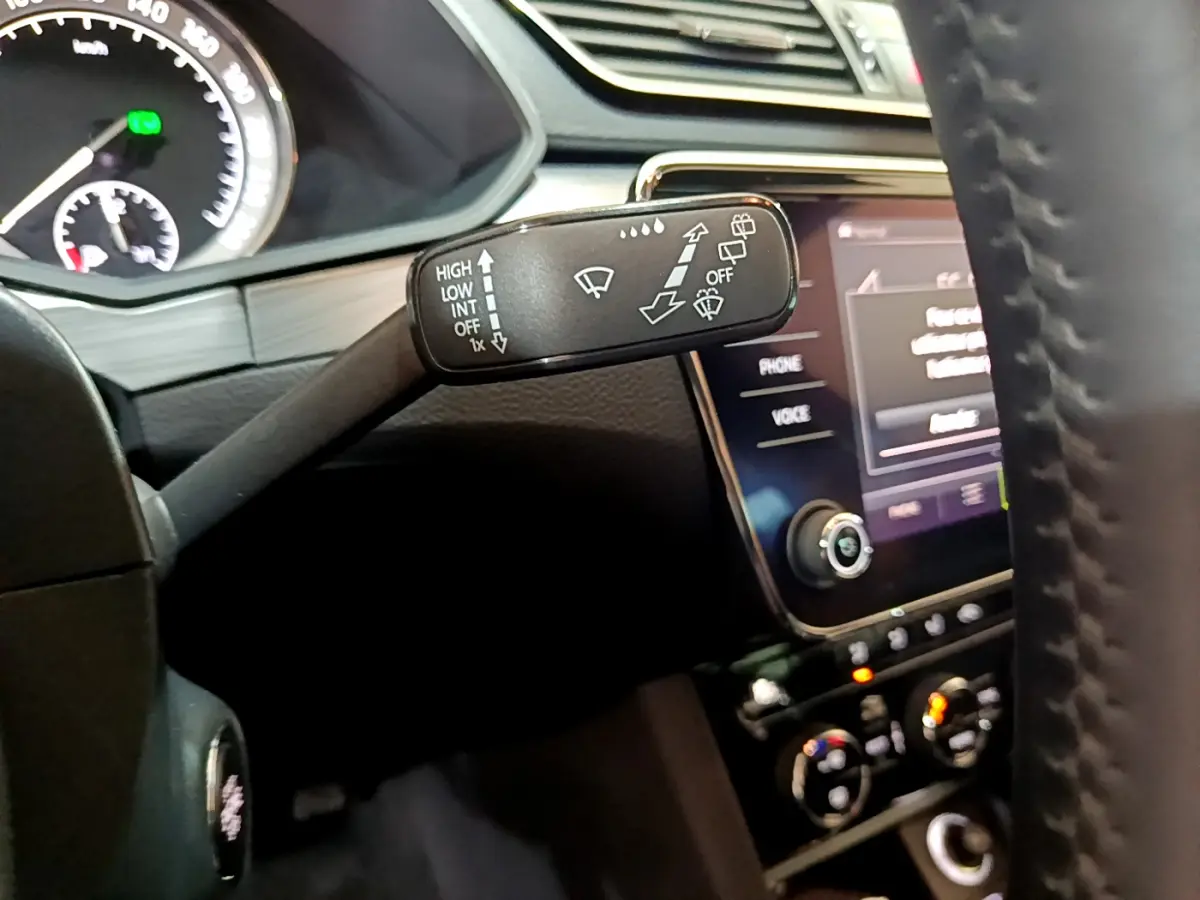 Gros plan sur la commande d’essuie-glace à gauche du volant cuir dans l’habitacle sombre d’une Skoda Superb gris clair.