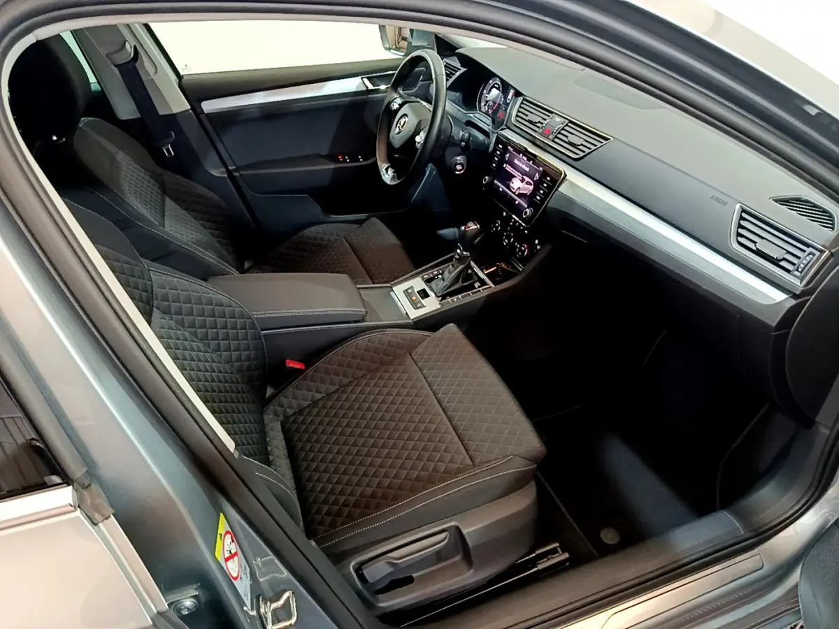 Intérieur de la Skoda Superb gris clair 2020 vu côté conducteur, sièges noirs matelassés et tableau de bord moderne avec écran tactile.